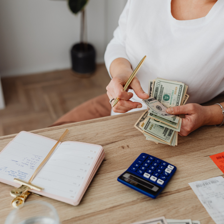 Woman sitting at a table counting money and budgeting with a notebook and calculator.