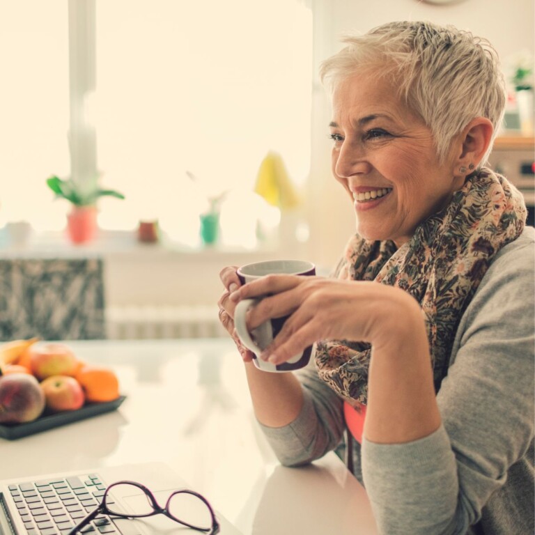 Happy woman enjoying coffee at home while using her laptop